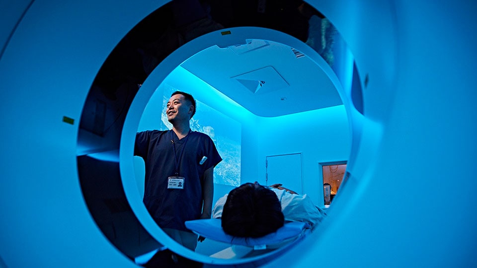 Photo of clinician setting up a scan at the CT scanner’s gantry, with the patient on the CT system’s patient table 